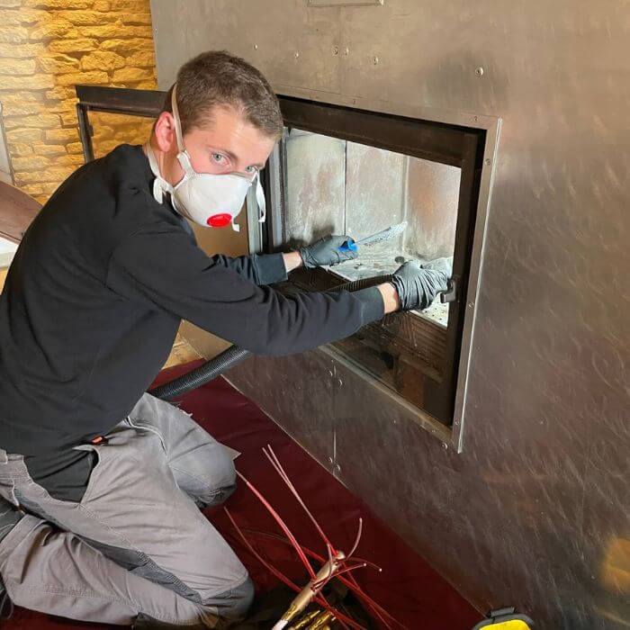 Technicien ramoneur nettoyant les arrivées d'air d'un conduit de cheminée, équipé d'un masque de protection.